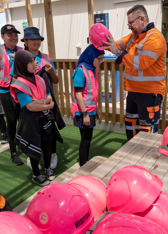 Photo of school kids wearing pink hard hats on site to support breast cancer
