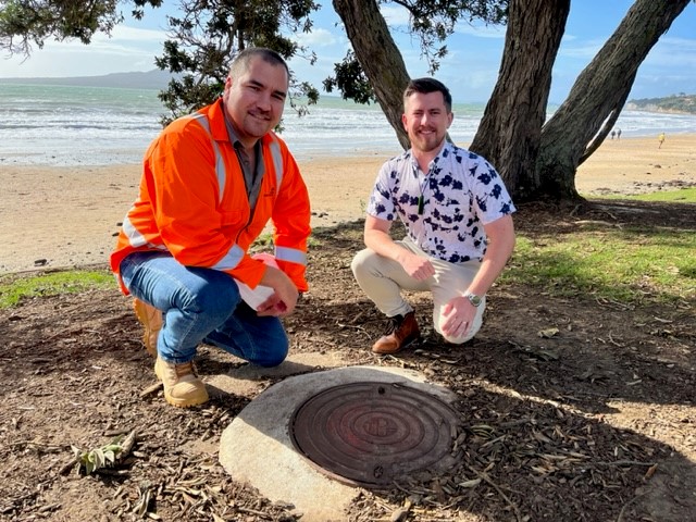 Photo of Watercare project manager Johan Gerritsen and Auckland Councillor Richard Hills kneel next to one of the manholes that was rehabilitated as part of the Takapuna Foreshore Beach Pipeline relining works